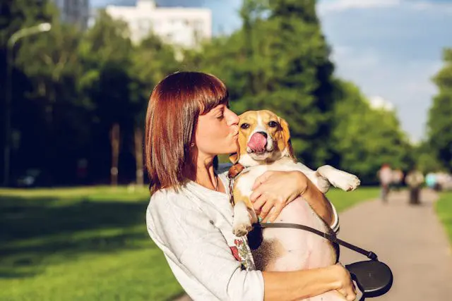 Woman kissing her dog in a park, highlighting the advantages of owning pets.