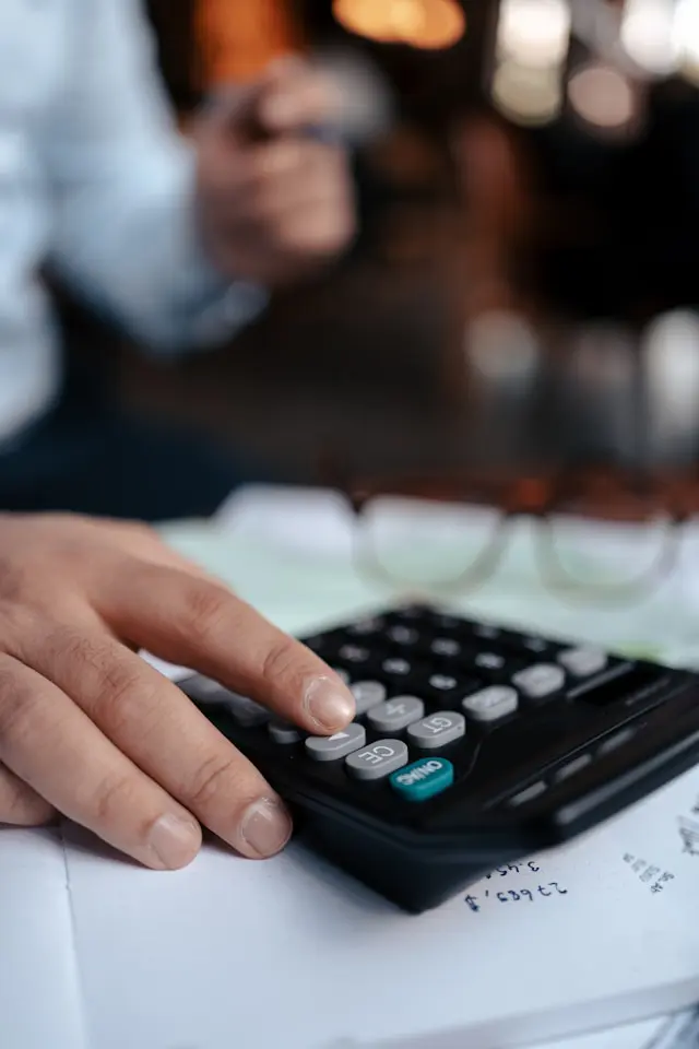 Person jotting down expenses in a calculator, categorizing spending in a home office.