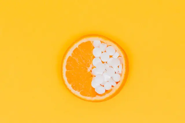 A slice of orange lies half filled with all-in-one vegan multivitamins on a yellow, orange background.