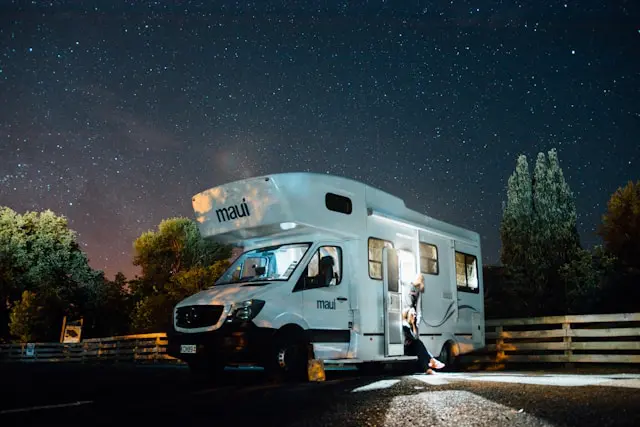 RV parked in a free parking lot under a starry night sky with a person standing by the door