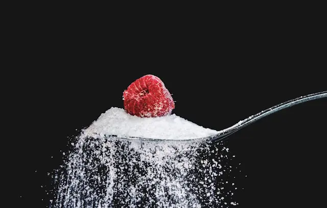 A raspberry on a spoon playfully pushing away sugar, symbolizing the fight against high blood sugar with fiber.