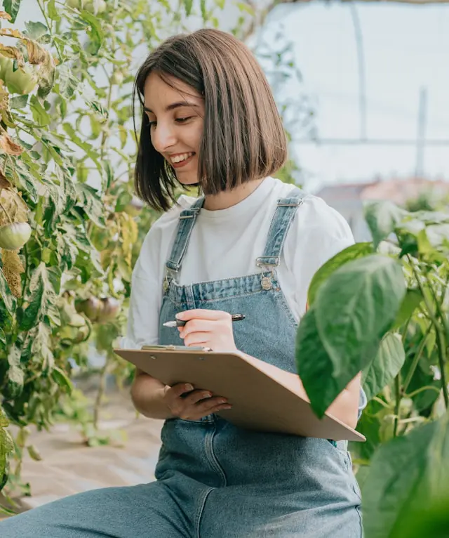 Female farmer taking notes in a greenhouse filled with plants.