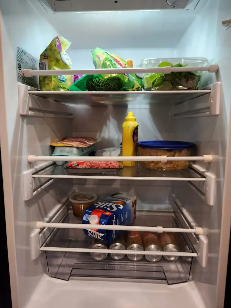 Well-organized RV fridge with vegetables, condiments, and other food items neatly arranged on shelves.