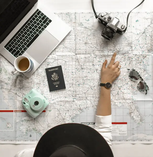 Person planning a trip with a map, passport, camera, and laptop