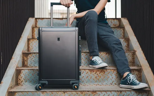 A young traveler sitting on industrial metal stairs with a sleek black suitcase, ready for a journey.