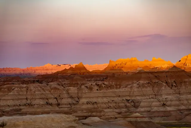 The soft glow of sunset illuminating the rugged landscape of Badlands National Park, enhancing the red and orange hues of the rock formations.