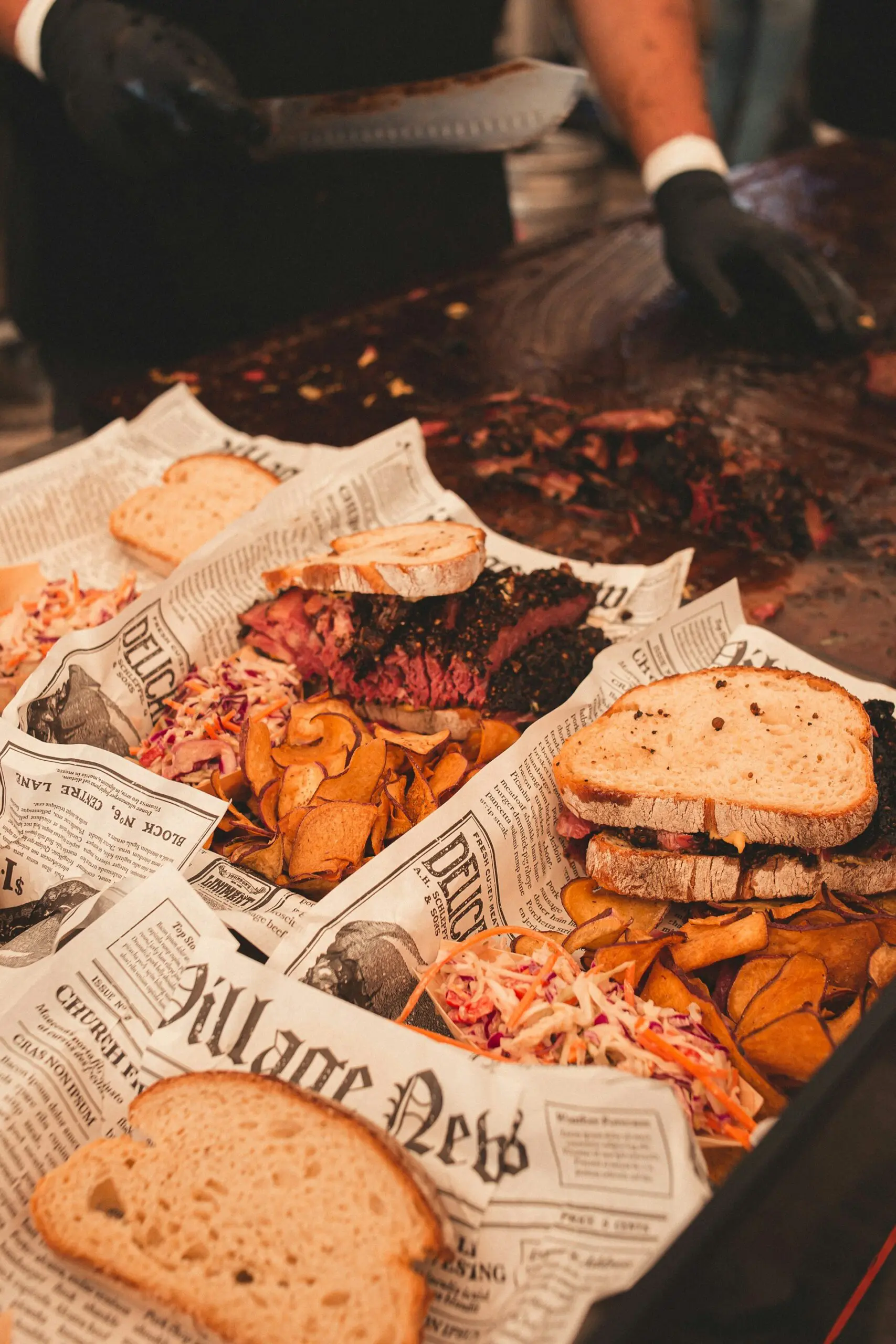 Gourmet BBQ sandwiches with brisket and coleslaw served on newspaper-lined trays, capturing a rustic dining style.