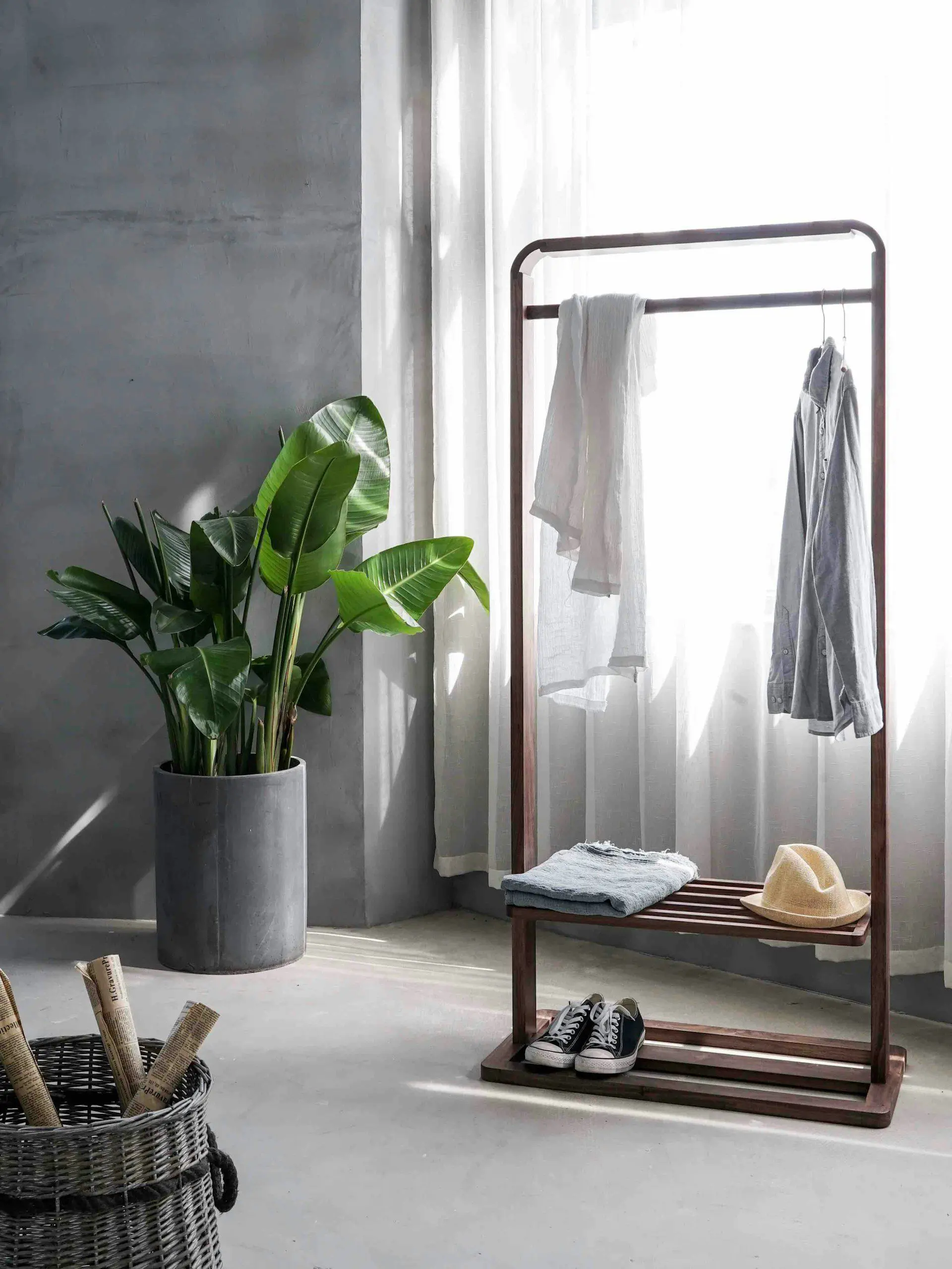 Gray dress shirt hanging on brown wooden rack in front of a window with white curtains showing minimal possessions