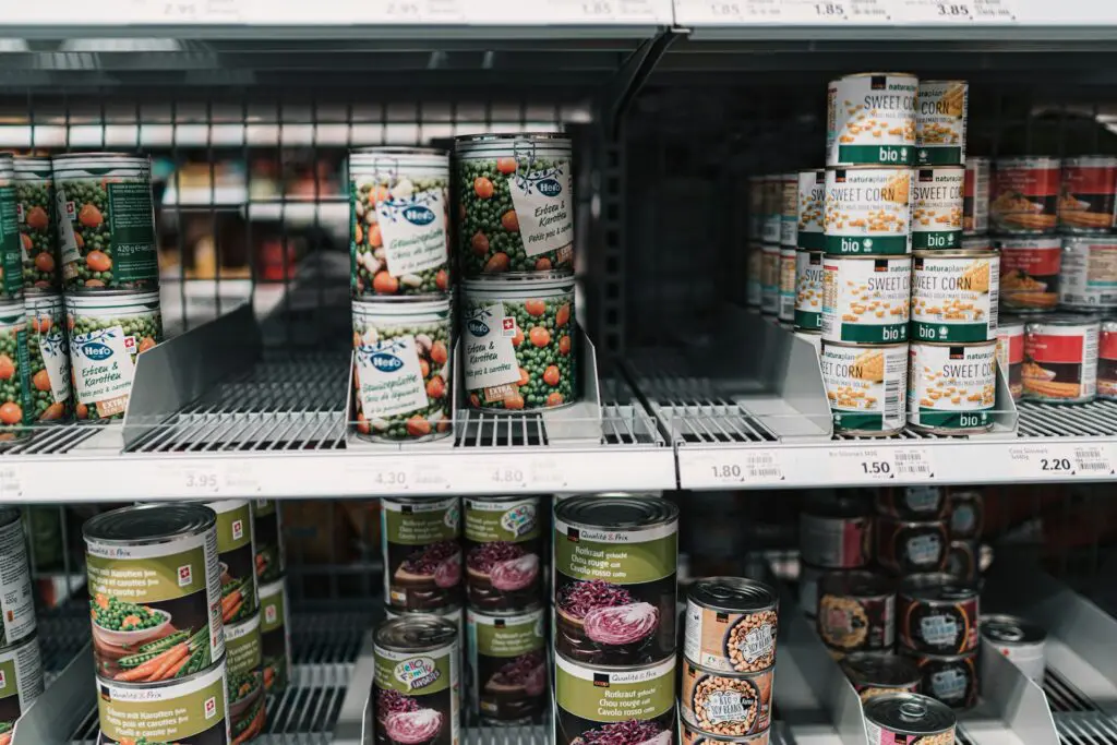 Rows of various canned vegetables, including peas, corn, and beets, displayed on grocery store shelves with clear pricing labels.