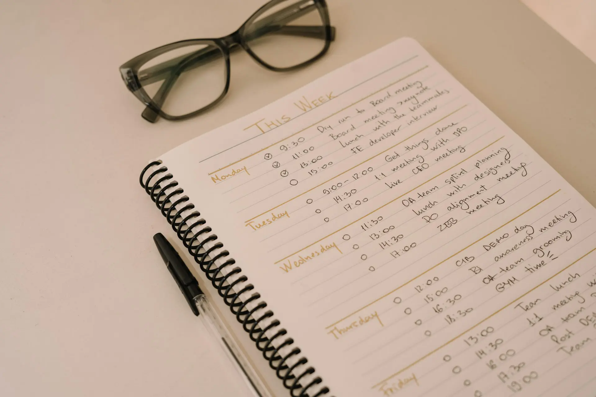 A detailed view of a weekly planner open to a page titled 'This Week' with handwritten schedule entries, glasses, and a pen.