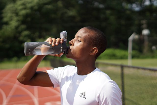 An athlete drinking water in a gym setting, highlighting the connection between hydration and muscle health.