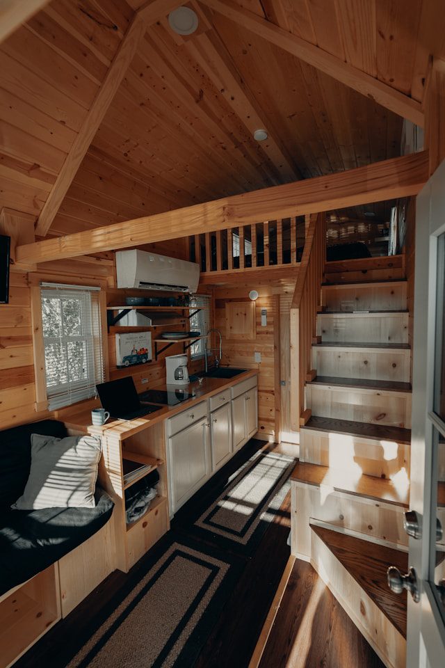 Cozy interior of a tiny house on wheels, featuring a small kitchen, built-in seating, and a loft area.