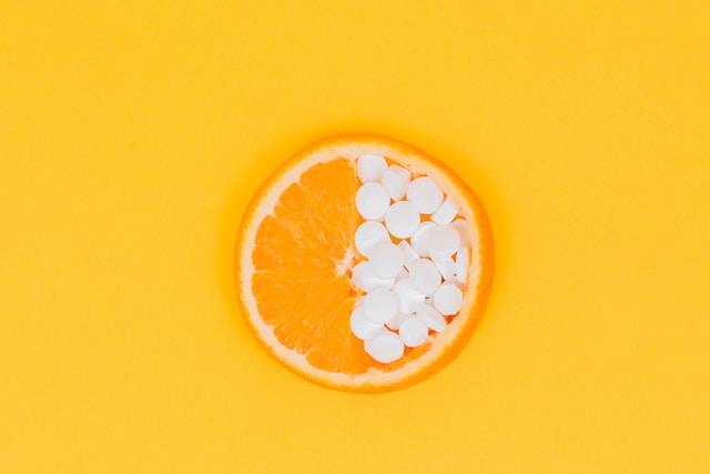 A slice of orange lies half filled with all-in-one vegan multivitamins on a yellow, orange background.