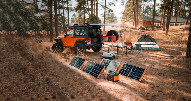 Jackery 1500W solar-powered generator and four portable solar panels in a rugged campsite with sun shining on the panels, showcasing some of the rv must-have for newbies