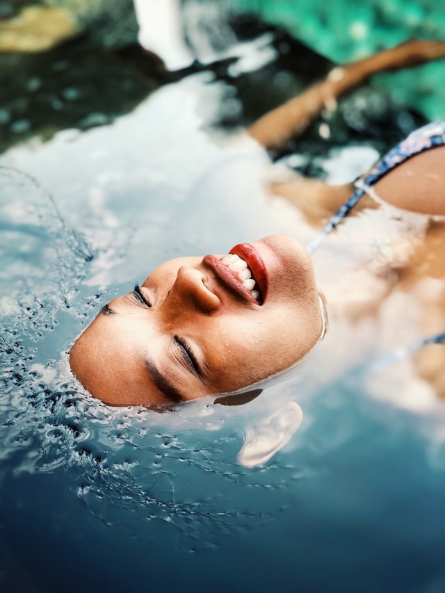 Person with glowing skin smiling while floating in water, illustrating the benefits of meditation for skin.