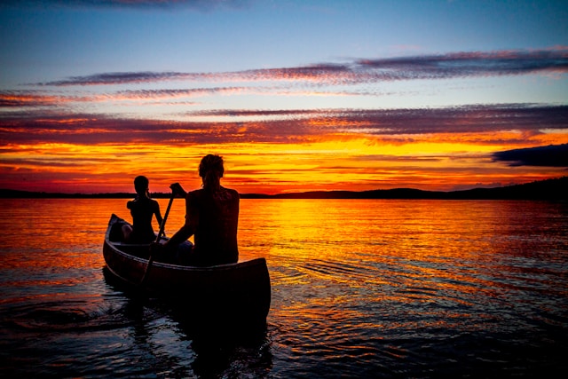 A peaceful, reflective scene at sunset with a two people in a canoe overlooking a tranquil lake, symbolizing contemplation.