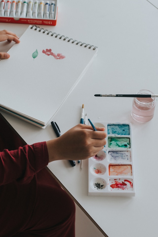 Close-up of hands holding paintbrushes, creating vibrant strokes on paper.