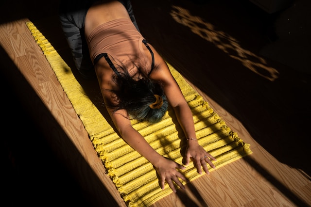 An adult relieving stress by resting on a yoga mat in a calm indoor setting with soft lighting