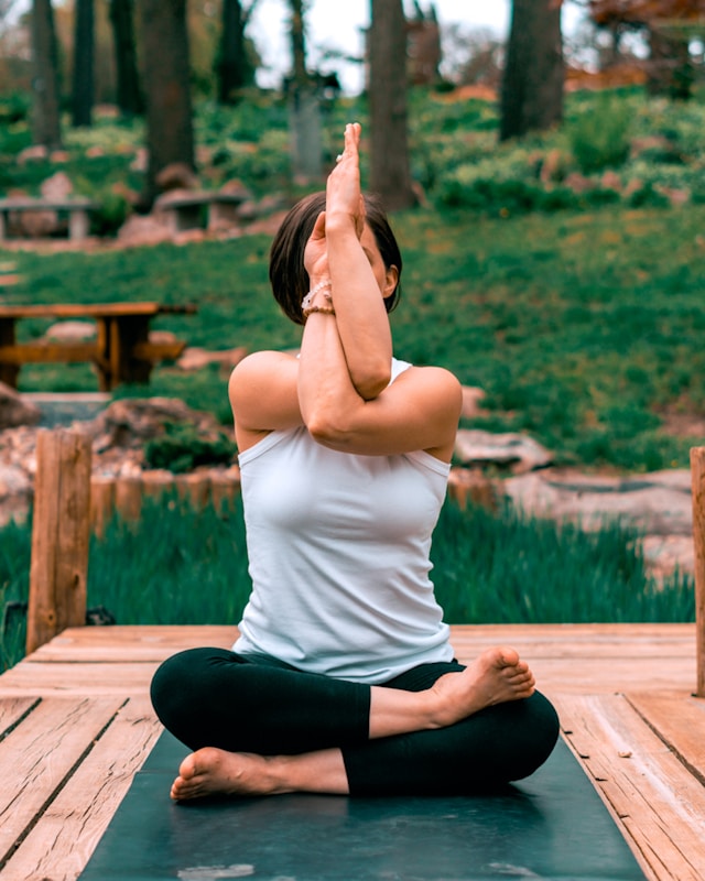 Person practicing yoga in a seated position outdoors, surrounded by lush greenery