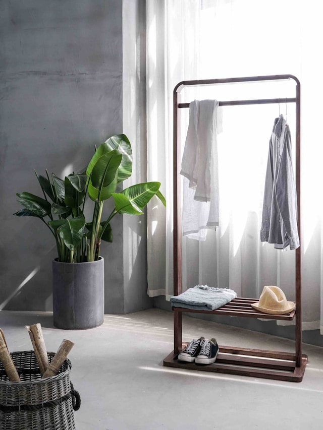 Gray dress shirt hanging on brown wooden rack in front of a window with white curtains showing minimal possessions