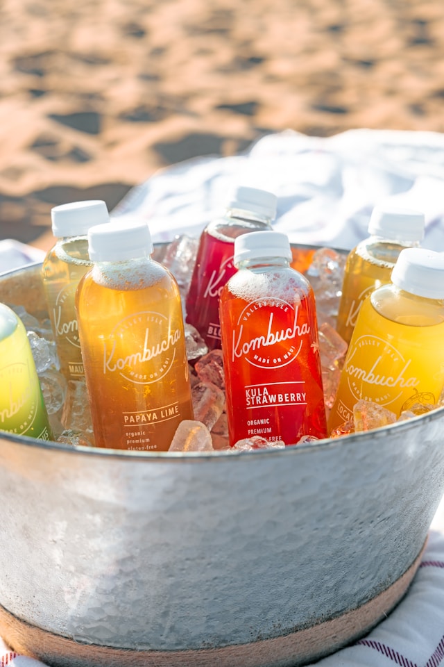 Artistically arranged bottles of kombucha with labels for flavors like papaya lime and kula strawberry, showcasing the variety from a kombucha brewing kit.