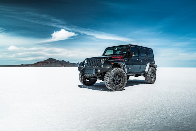 Black Jeep Wrangler with oversized tires driving on salt flats under a blue sky