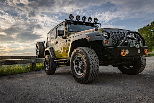 Green Jeep Wrangler with mounted light bar and rugged tires in a scenic outdoor setting