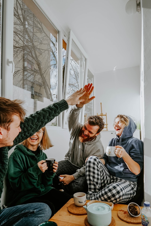 Group of friends laughing and enjoying a casual gathering without alcohol, showing support and camaraderie in a bright, cozy room