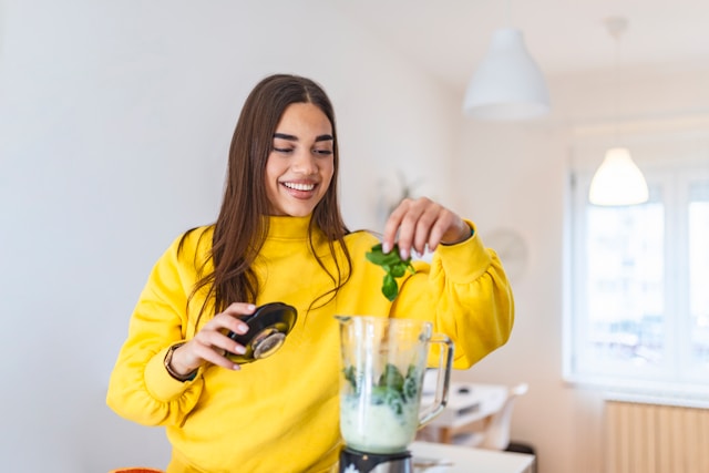 Young woman adding spinach to blender for gut-healing smoothie