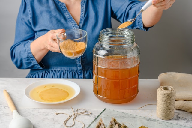 Person adding sugar to a jar of kombucha brew during the brewing process