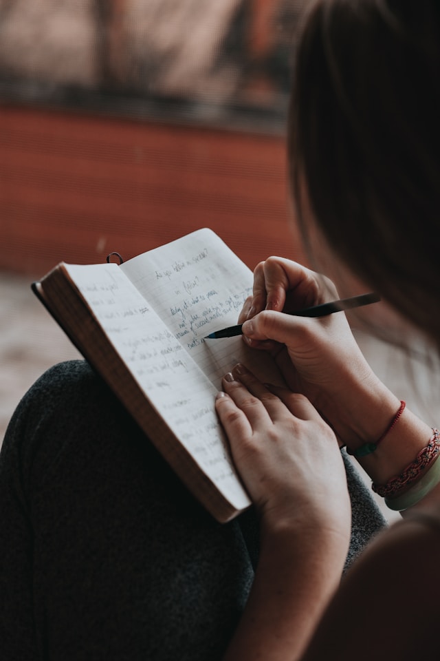 Close-up of a person writing in a journal, with a focus on the hands and pen.