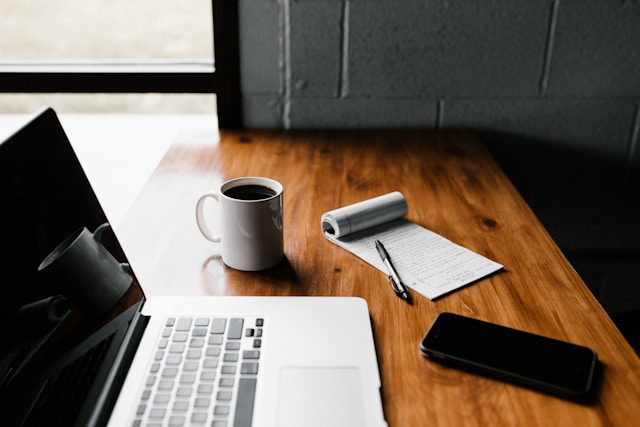 A desk setup with a laptop, coffee, and a journal