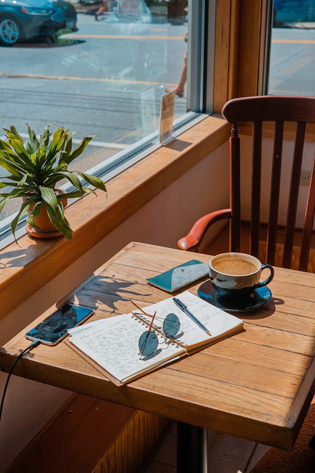 Cozy cafe spot with a journal, coffee, and sunglasses