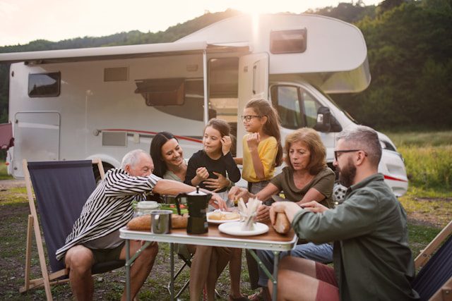 Family enjoying a meal at a camping site with an RV in the background.