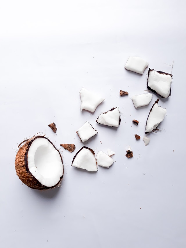 Chunks of fresh coconut scattered on a white background, with a halved coconut shell.