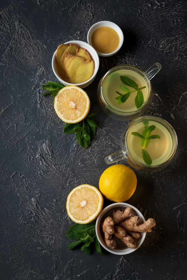 A top view of a table with ginger, lemon, mint leaves, and cups of ginger lemon tea arranged neatly.