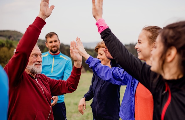 A group of people outdoors, smiling and giving high-fives to each other, showing a sense of community and achievement.