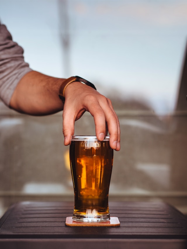 Hand reaching for a glass of beer on a table.