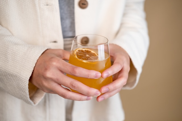 Person holding a glass of kombucha with a slice of dried lemon