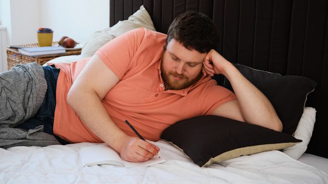 Man lying on bed and journaling to manage anxiety