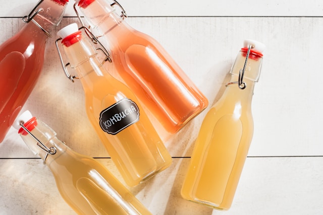 Bottles of homemade kombucha in different colors on a white background