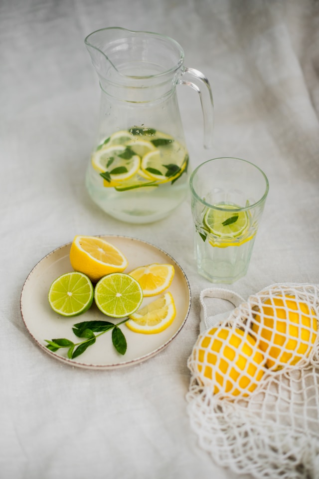 A pitcher and glass of lemon and lime-infused water on a table with fresh lemons and limes.