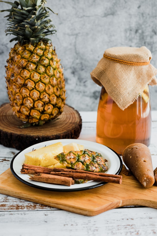 Jar of pineapple cinnamon kombucha next to a fresh pineapple and cinnamon sticks