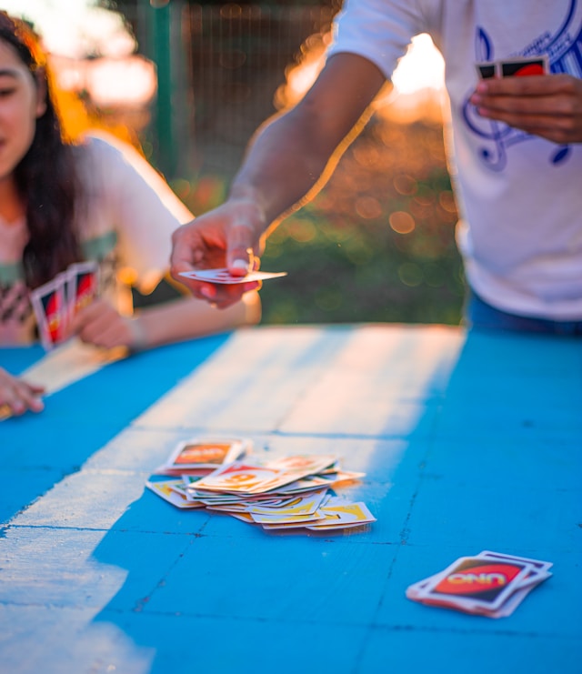 Campers playing a card game on a picnic table at sunset.