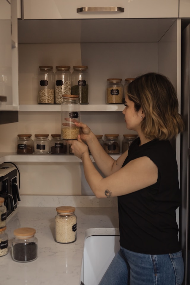 Woman organizing a pantry in an RV with labeled glass jars containing various dry goods on shelves