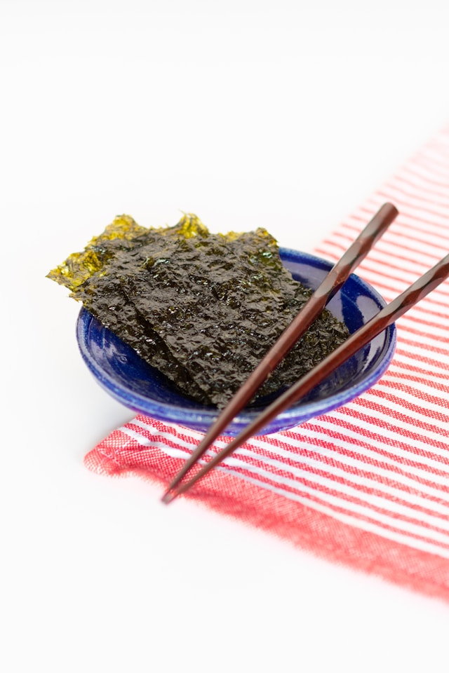 A blue bowl filled with seaweed crisps, placed on a red and white striped napkin with chopsticks resting on the bowl.