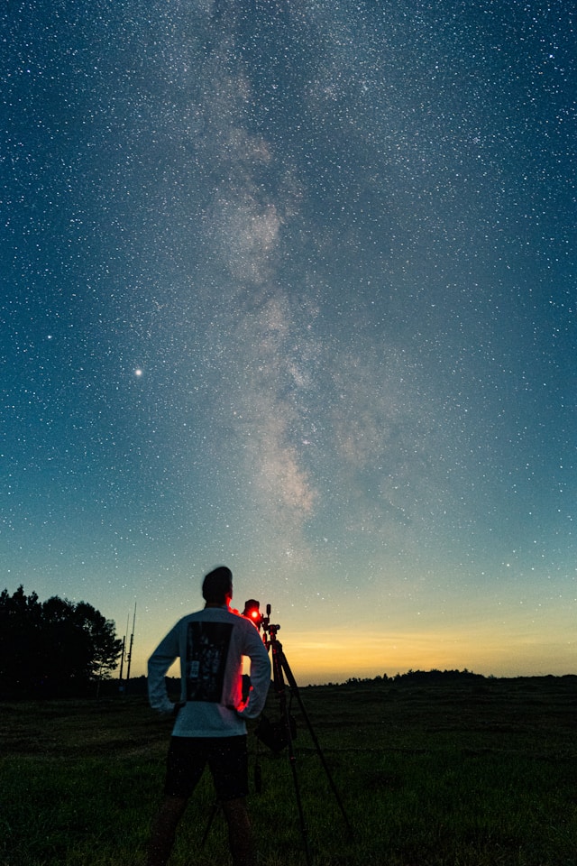 Person stargazing with a telescope at a campsite under a clear night sky.