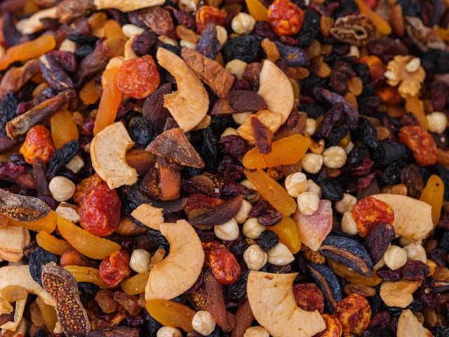 A close-up view of a colorful mix of dried fruits and nuts, including apricots, apples, raisins, hazelnuts, and other assorted dried fruits and nuts.