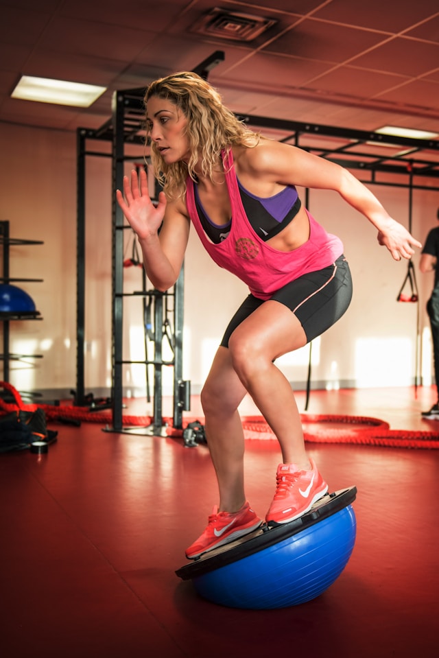 Woman performing a balance exercise on a Bosu ball in a gym.