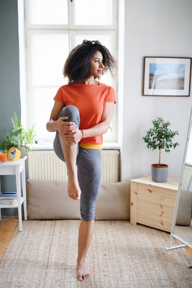 Young woman performing a yoga pose in her living room, representing wellness practices that complement acupuncture.